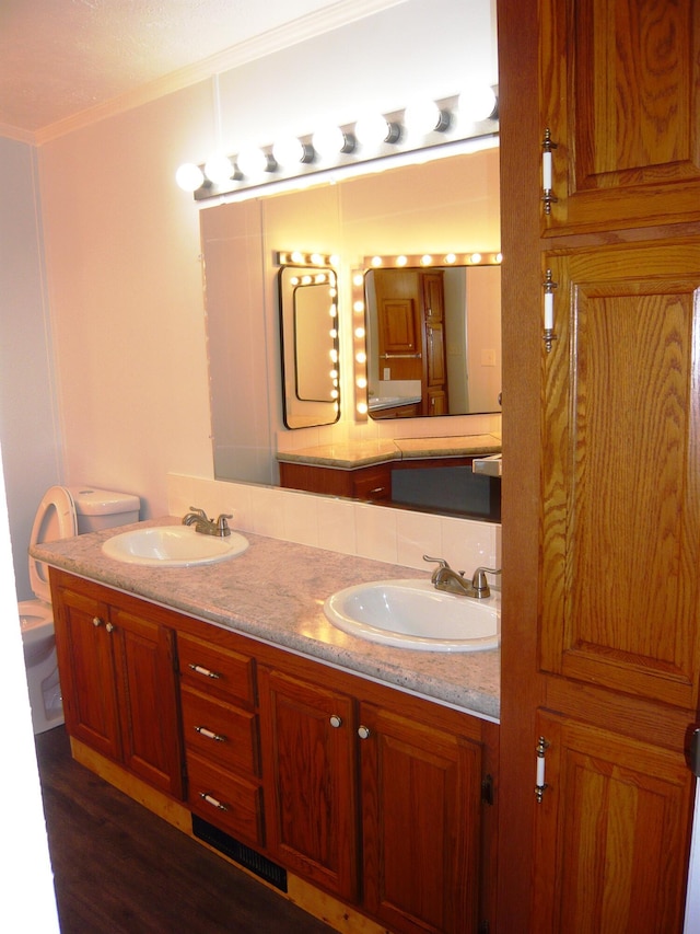 full bathroom featuring crown molding, wood finished floors, double vanity, and a sink