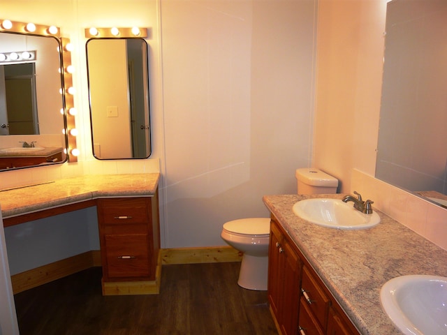 full bath with toilet, wood finished floors, double vanity, and a sink