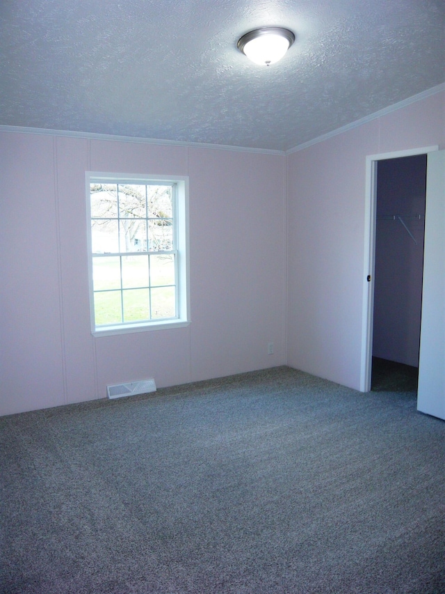 spare room with a textured ceiling, carpet flooring, crown molding, and visible vents