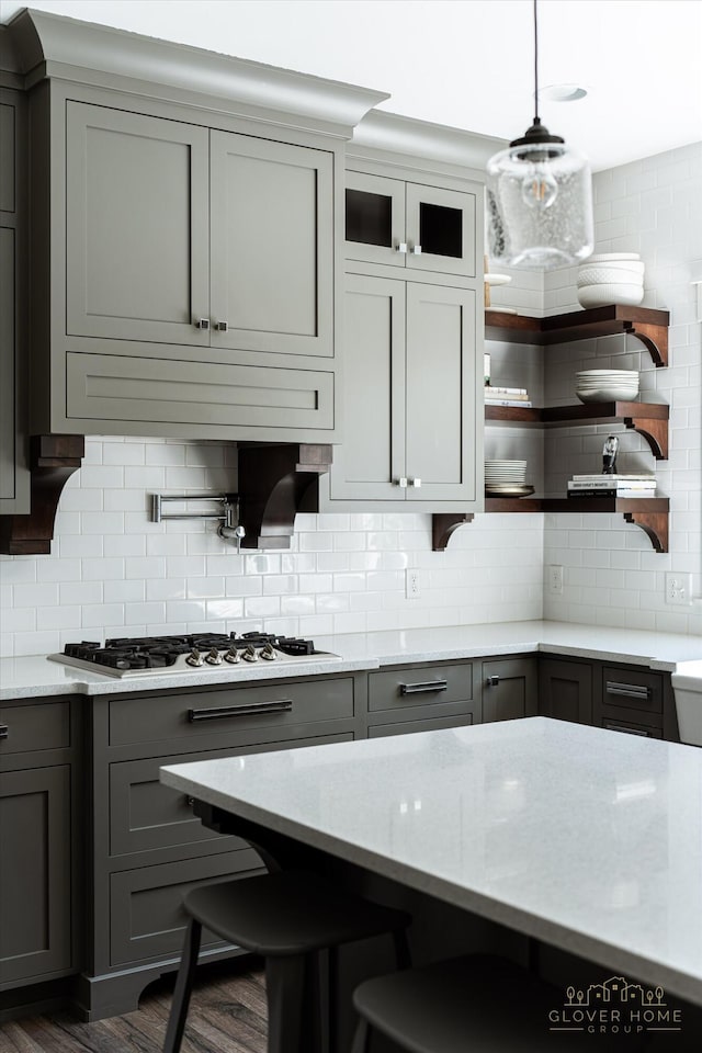 kitchen with stainless steel gas stovetop, open shelves, light stone counters, gray cabinetry, and backsplash