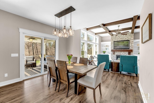 dining area featuring wood finished floors, baseboards, a ceiling fan, and a stone fireplace