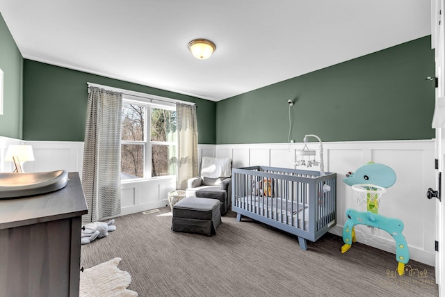 bedroom with a crib, a decorative wall, carpet, and a wainscoted wall