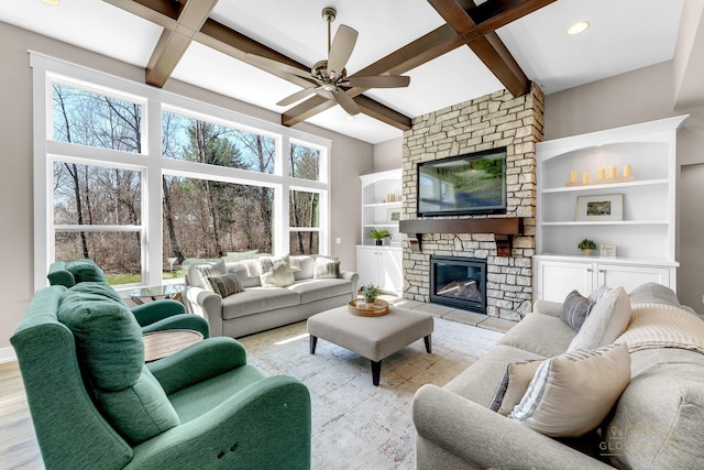 living room with a stone fireplace, beamed ceiling, coffered ceiling, and ceiling fan