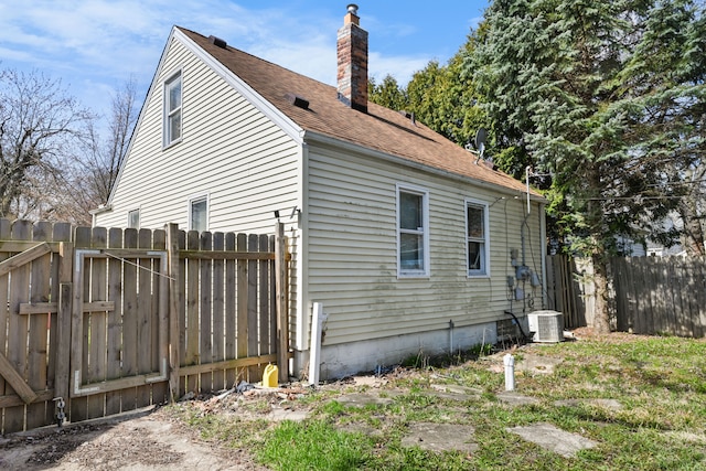 view of side of property with fence, central AC, and a chimney