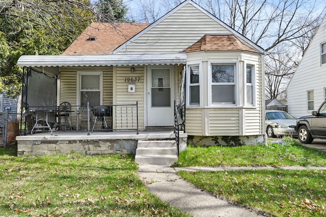 bungalow-style house featuring a front lawn, covered porch, and roof with shingles
