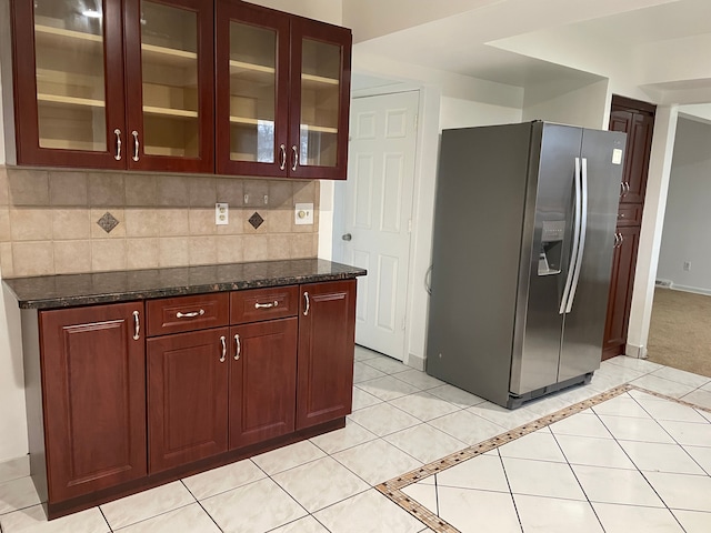 kitchen with stainless steel fridge with ice dispenser, glass insert cabinets, tasteful backsplash, light tile patterned floors, and dark stone counters