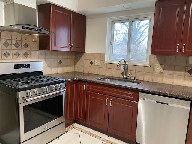 kitchen with dark stone counters, wall chimney exhaust hood, tasteful backsplash, appliances with stainless steel finishes, and a sink