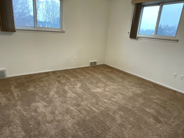 unfurnished room with carpet, visible vents, and baseboards
