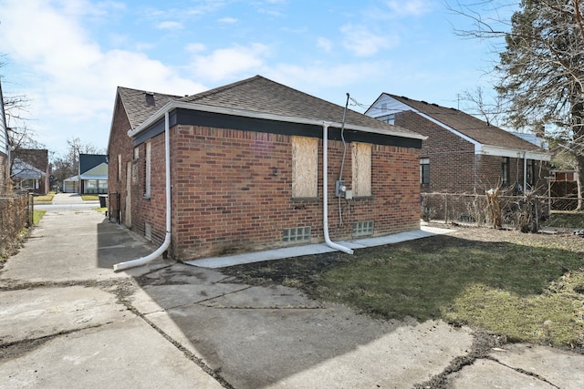 view of side of home featuring brick siding, fence, and roof with shingles