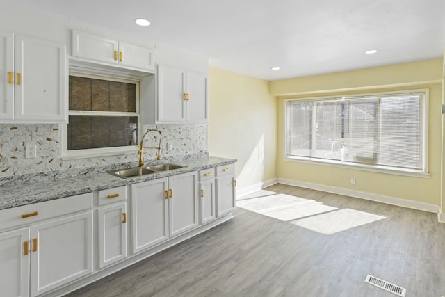 kitchen featuring tasteful backsplash, white cabinets, a sink, baseboards, and light wood-type flooring