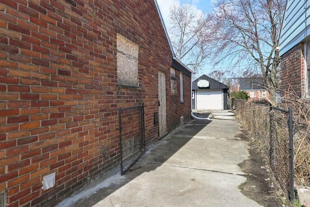 view of property exterior featuring an outdoor structure, brick siding, fence, a garage, and driveway