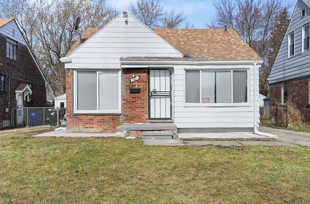 bungalow featuring brick siding, fence, a shingled roof, and a front yard