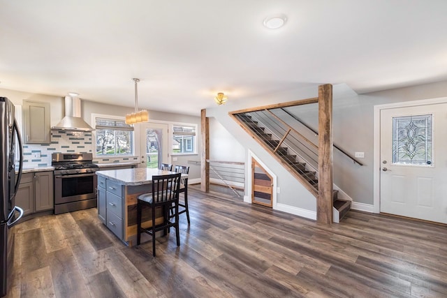 kitchen featuring wall chimney exhaust hood, dark wood-style floors, a kitchen bar, and stainless steel gas range oven