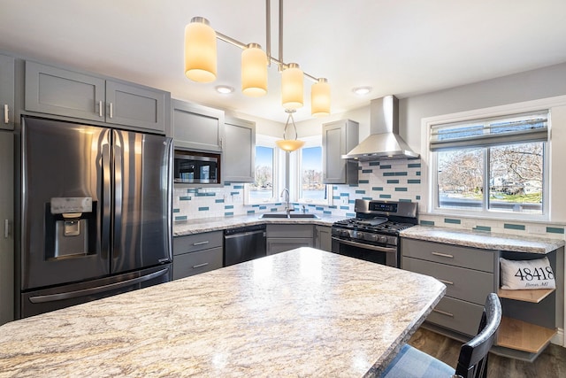 kitchen with gray cabinets, stainless steel appliances, wall chimney range hood, backsplash, and a sink