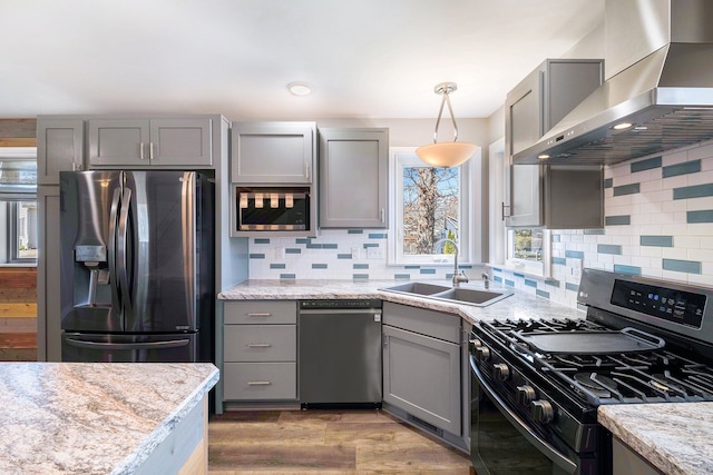 kitchen featuring a sink, light wood finished floors, wall chimney exhaust hood, appliances with stainless steel finishes, and gray cabinetry