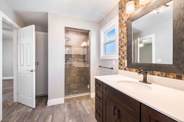 bathroom with baseboards, a ceiling fan, wood finished floors, a shower stall, and vanity