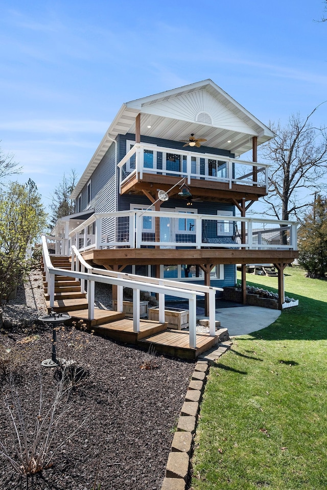 rear view of property with a yard, a wooden deck, a balcony, a ceiling fan, and stairs