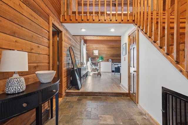 hall featuring stone tile floors, wooden walls, recessed lighting, and baseboards