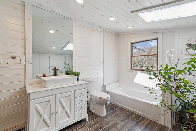 bathroom with a skylight, wood finished floors, a bathing tub, toilet, and vanity