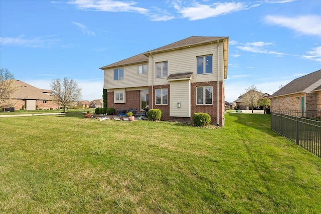 rear view of house featuring a lawn, brick siding, and fence