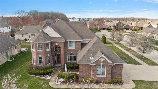 view of front of property with a shingled roof, brick siding, a front yard, and a residential view