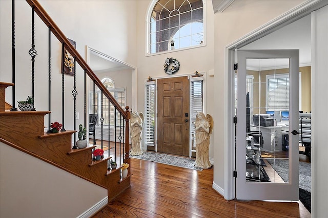 foyer with stairway, a towering ceiling, wood finished floors, crown molding, and baseboards