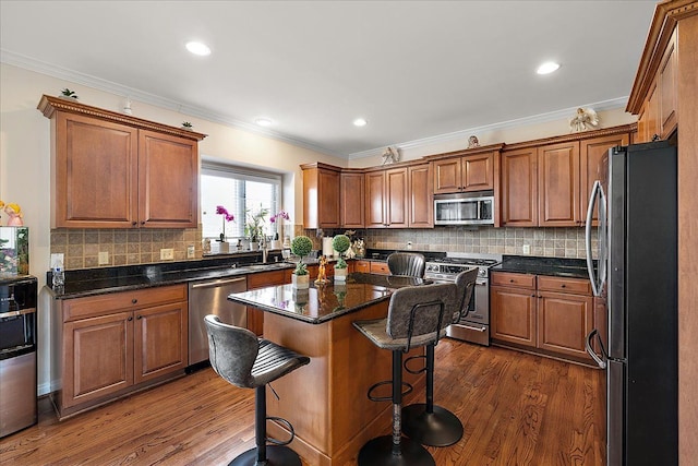 kitchen featuring crown molding, a kitchen breakfast bar, appliances with stainless steel finishes, and dark wood-style flooring