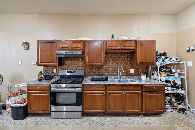 kitchen with under cabinet range hood, stainless steel gas range oven, stone countertops, a sink, and tasteful backsplash