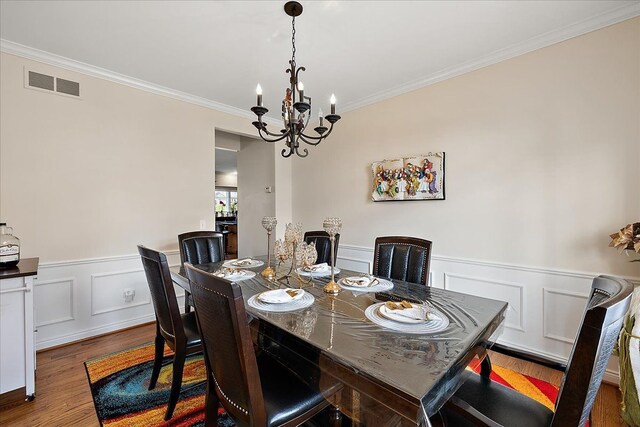 dining space featuring a wainscoted wall, wood finished floors, visible vents, crown molding, and a chandelier