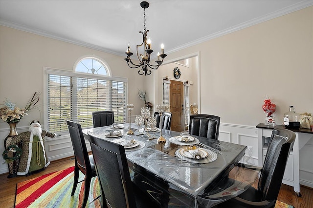 dining area with wood finished floors, a decorative wall, crown molding, wainscoting, and a notable chandelier