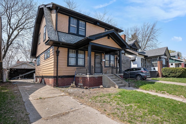 bungalow-style home featuring an outdoor structure, a shingled roof, a front lawn, and covered porch