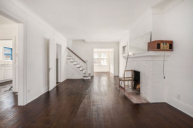 unfurnished living room featuring dark wood-style floors, a sink, baseboards, stairway, and a fireplace