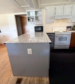 kitchen featuring white cabinets, a peninsula, wood finished floors, and white gas range