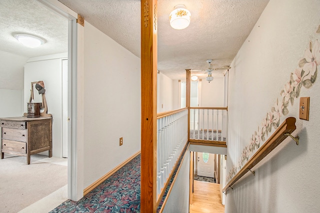 hall with a textured ceiling, baseboards, an upstairs landing, and carpet floors