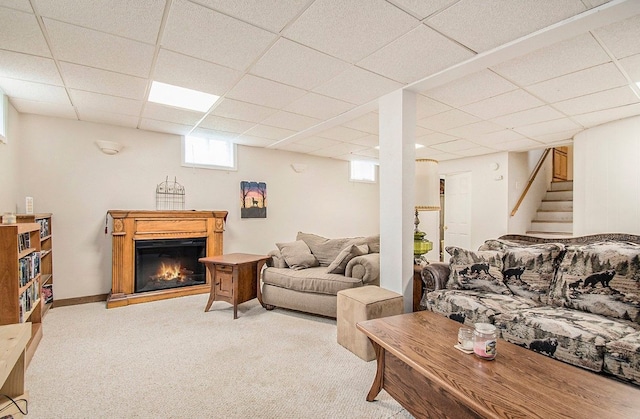 living area featuring carpet floors, a paneled ceiling, a glass covered fireplace, and stairs