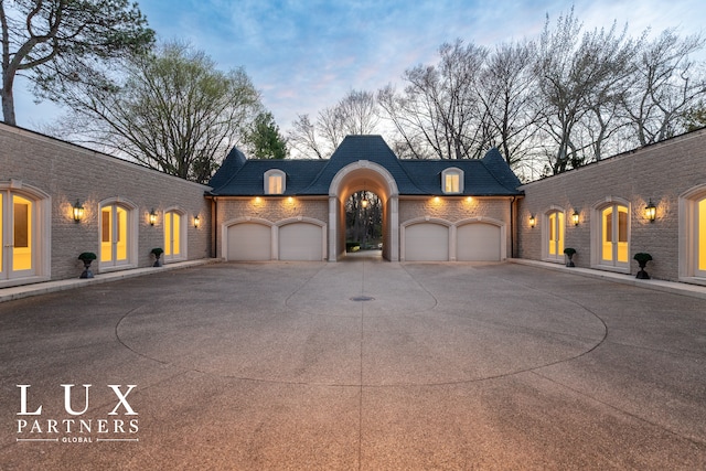 view of front of home featuring concrete driveway, an attached garage, brick siding, and a high end roof