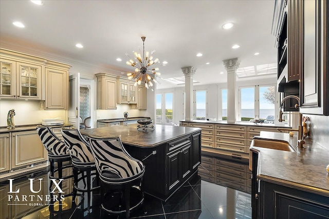 kitchen with dark countertops, dark cabinetry, cream cabinetry, ornate columns, and a kitchen island