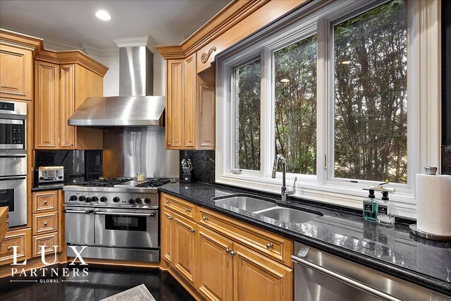 kitchen with dark stone countertops, wall chimney range hood, a sink, tasteful backsplash, and appliances with stainless steel finishes