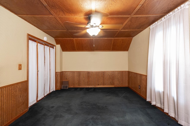 bonus room featuring dark colored carpet, ceiling fan, wainscoting, wood walls, and lofted ceiling