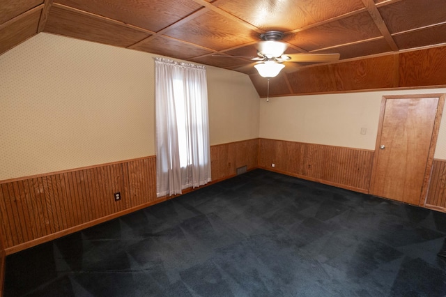 additional living space featuring ceiling fan, a wainscoted wall, lofted ceiling, wooden walls, and dark colored carpet