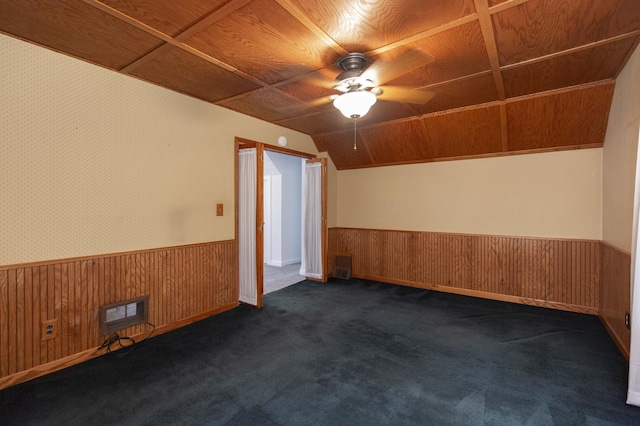 unfurnished room with wooden walls, dark carpet, a wainscoted wall, and ceiling fan