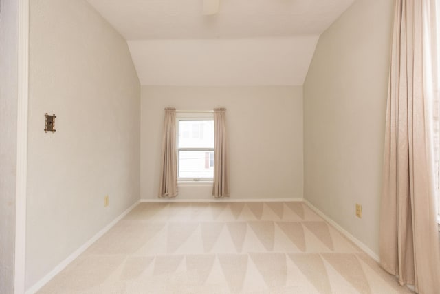 spare room featuring light colored carpet, baseboards, and lofted ceiling