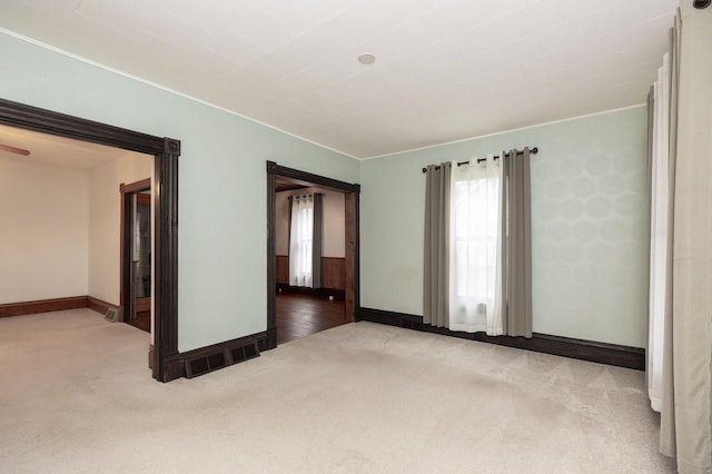empty room featuring carpet, visible vents, baseboards, and ornamental molding