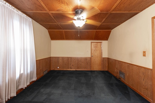 bonus room featuring wood walls, wainscoting, dark carpet, and ceiling fan
