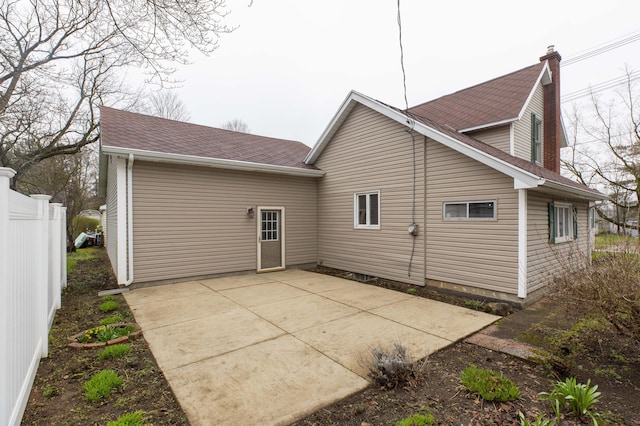 back of property with a patio, a chimney, fence, and a shingled roof