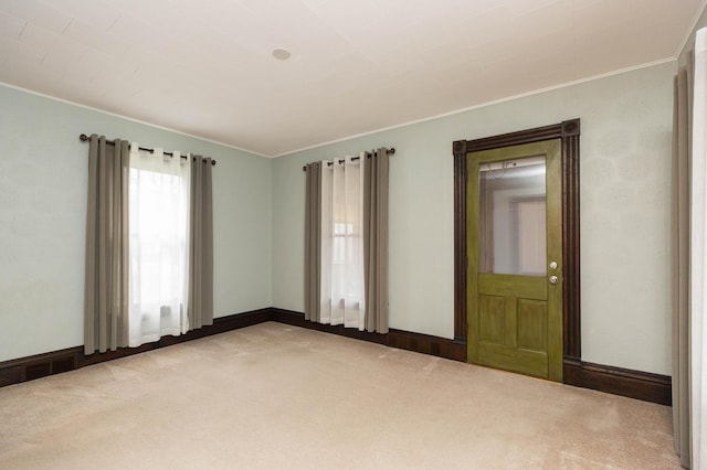 carpeted empty room featuring crown molding and baseboards