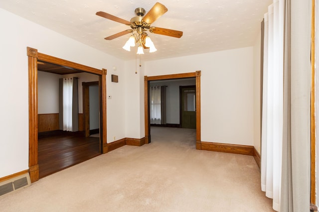 empty room featuring light carpet, visible vents, baseboards, and a ceiling fan