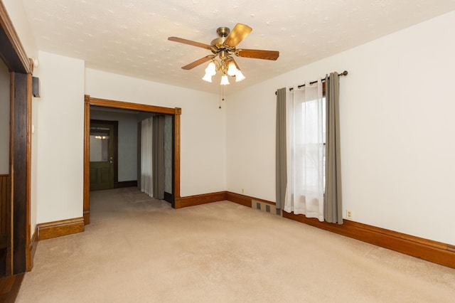 empty room featuring a textured ceiling, light colored carpet, baseboards, and ceiling fan