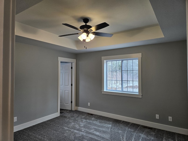spare room with visible vents, baseboards, dark carpet, and a ceiling fan