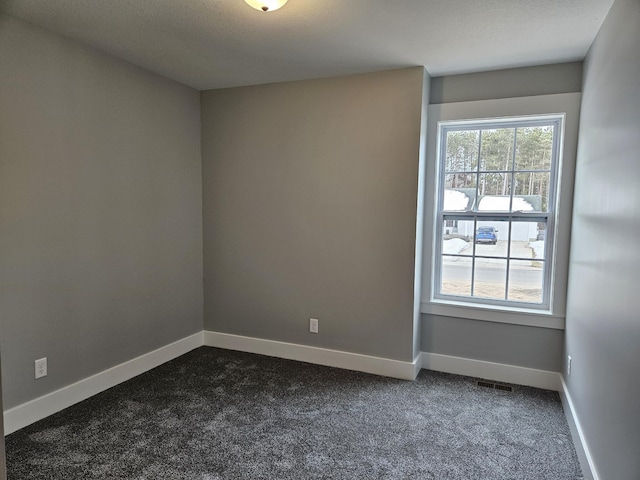 spare room featuring dark carpet, baseboards, and visible vents